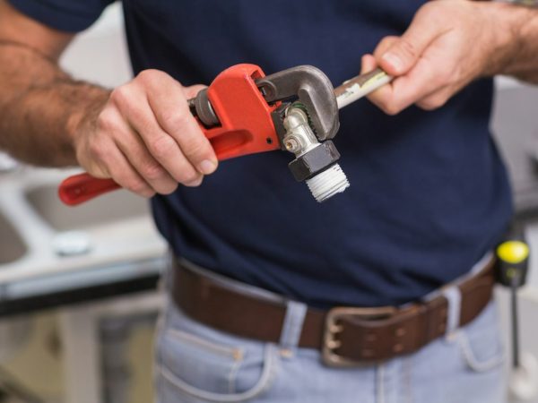 plumber-fixing-pipe-with-wrench-in-the-kitchen.jpg
